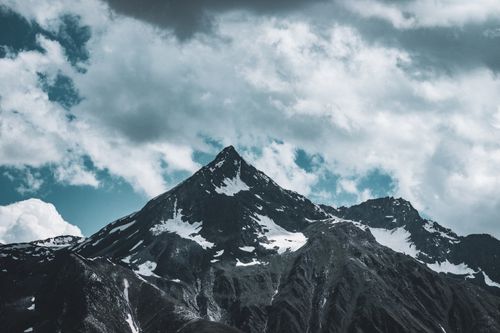 Free Snow-capped mountain peak beneath dramatic clouds, perfect for adventure and nature themes. Stock Photo