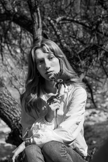 Black and white portrait of a young woman holding a flower in an outdoor setting.