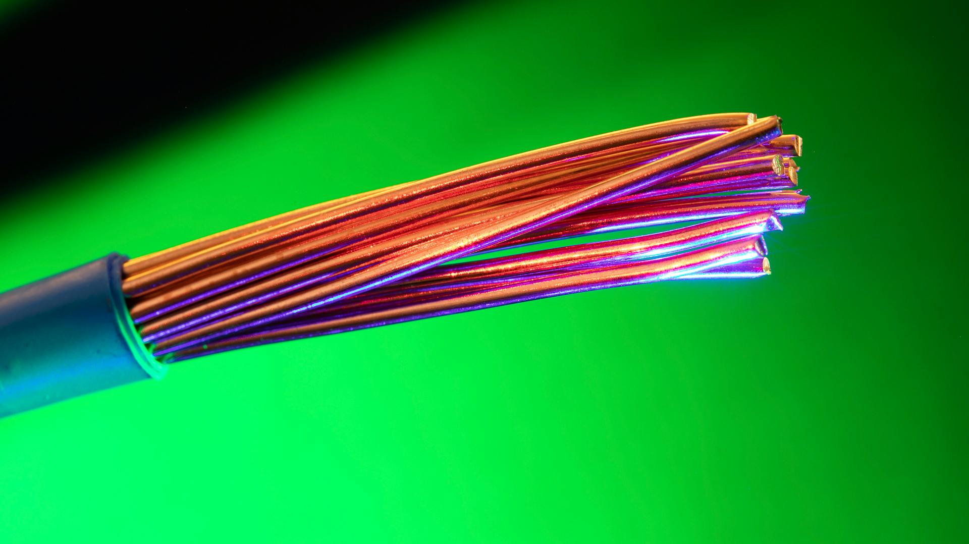 Close-up of colorful copper electrical wires against a vibrant green backdrop, showcasing vivid contrasts and textures.