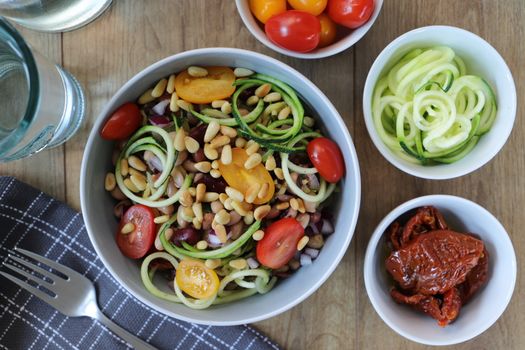 Fresh zucchini noodle salad topped with tomatoes and pine nuts for a healthy meal.