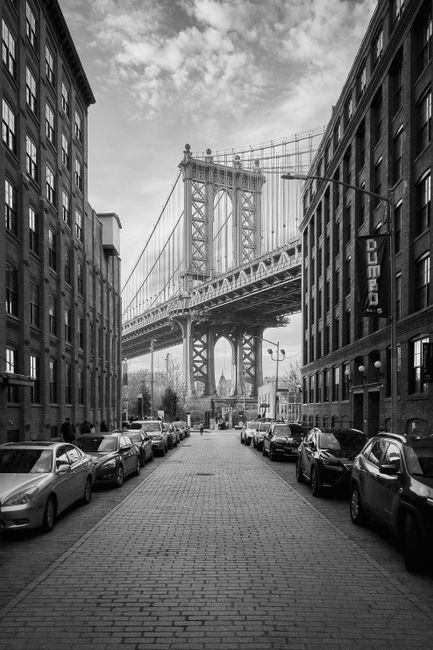 Black and white photograph of Manhattan Bridge framed by city streets in Brooklyn, New York City.