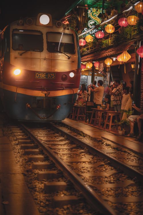 Free A train moves through a lively street cafe adorned with colorful lanterns at night. Stock Photo