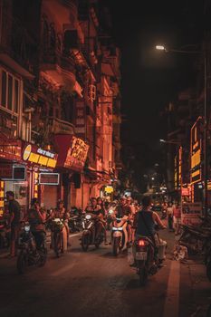 Nighttime city street scene filled with motorbikes under warm street lights.