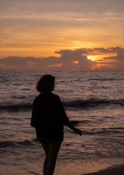 A peaceful silhouette of a person standing on a beach with a vibrant sunset in the background.