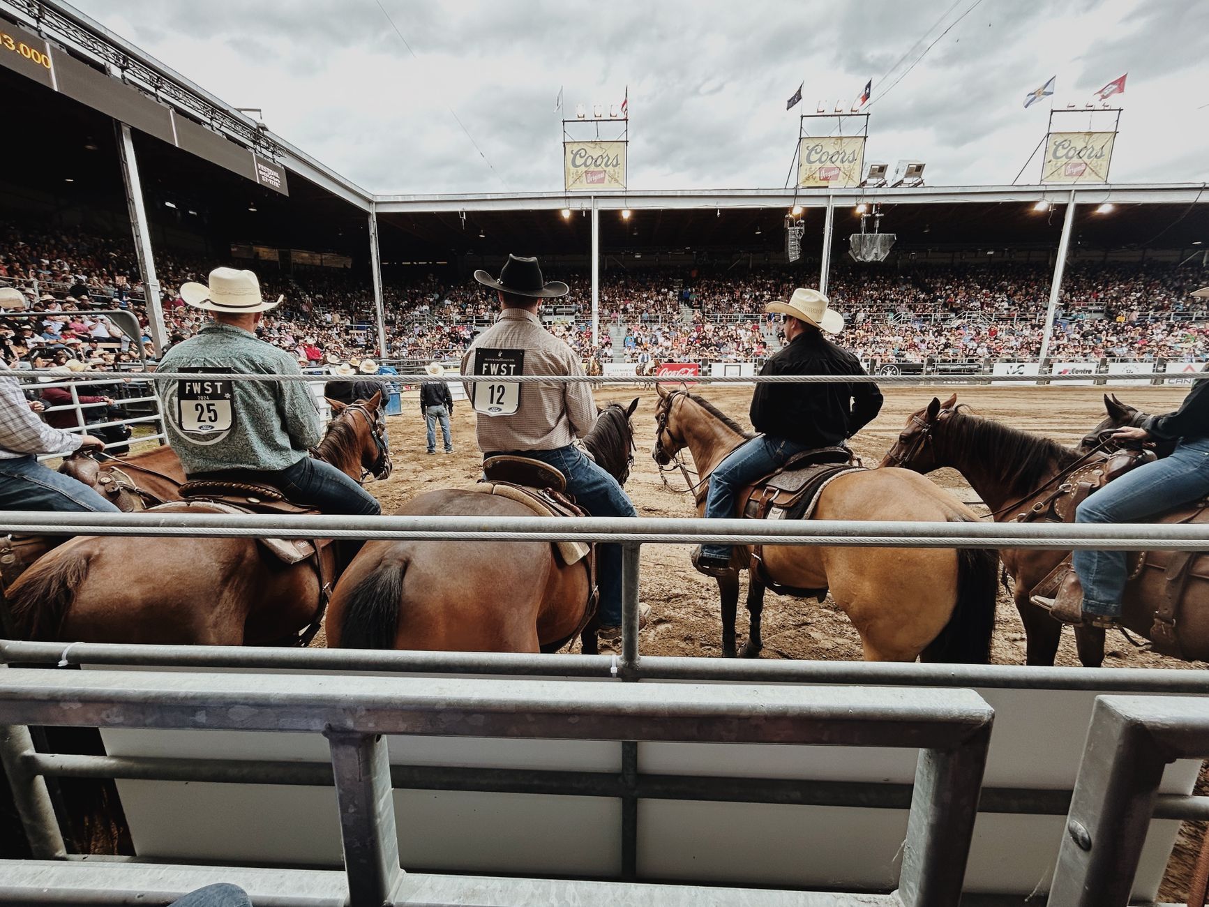 Group of cowboys on horseback at a rodeo event in an outdoor stadium.