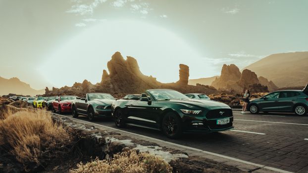 Cars lined up on a scenic road with striking rock formations during sunset.