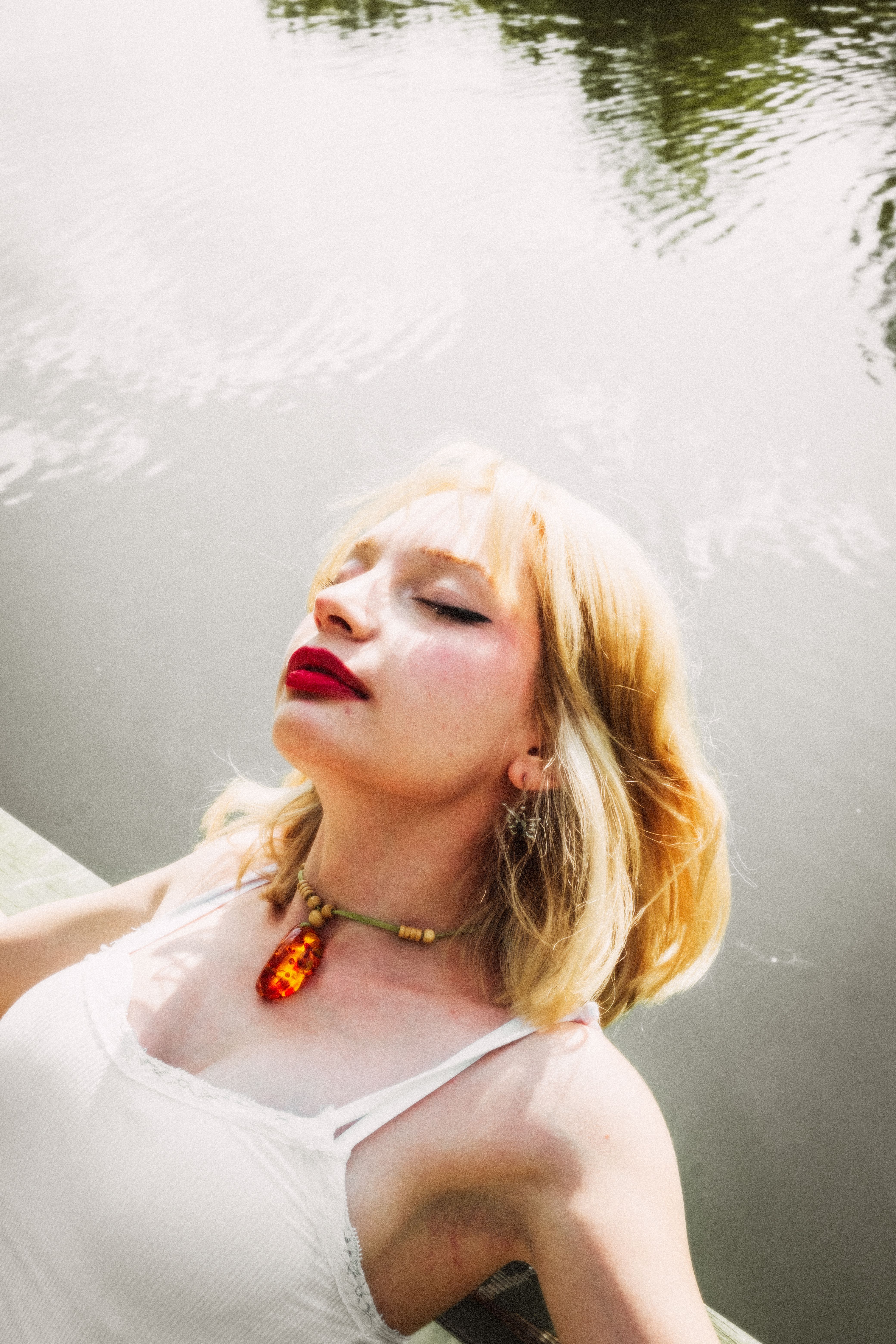 A woman in a white dress enjoys a peaceful moment by the water under the summer sun.