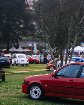 Colorful scene at a classic car show with a prominent red sports car and vintage vehicles.