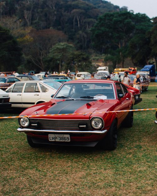 Free A vibrant red vintage car displayed at an outdoor auto show surrounded by lush greenery. Stock Photo