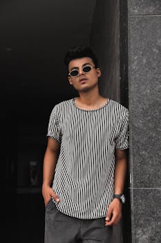 一位时尚的年轻人戴着墨镜，身穿条纹衬衫，在户外摆出姿势，传达出现代时尚的氛围