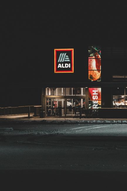 A nighttime winter view of an Aldi storefront with a prominent logo, captured in Roeland Park, KS. A nighttime winter view of an Aldi storefront with a prominent logo, captured in Roeland Park, KS.