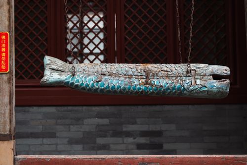 Free A rustic wooden fish sculpture suspended on chains, set against a lattice-patterned wall, evoking traditional Asian aesthetics. Stock Photo