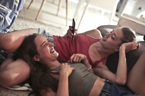 Free Two young women smiling and laughing while relaxing indoors, capturing a moment of friendship and happiness. Stock Photo