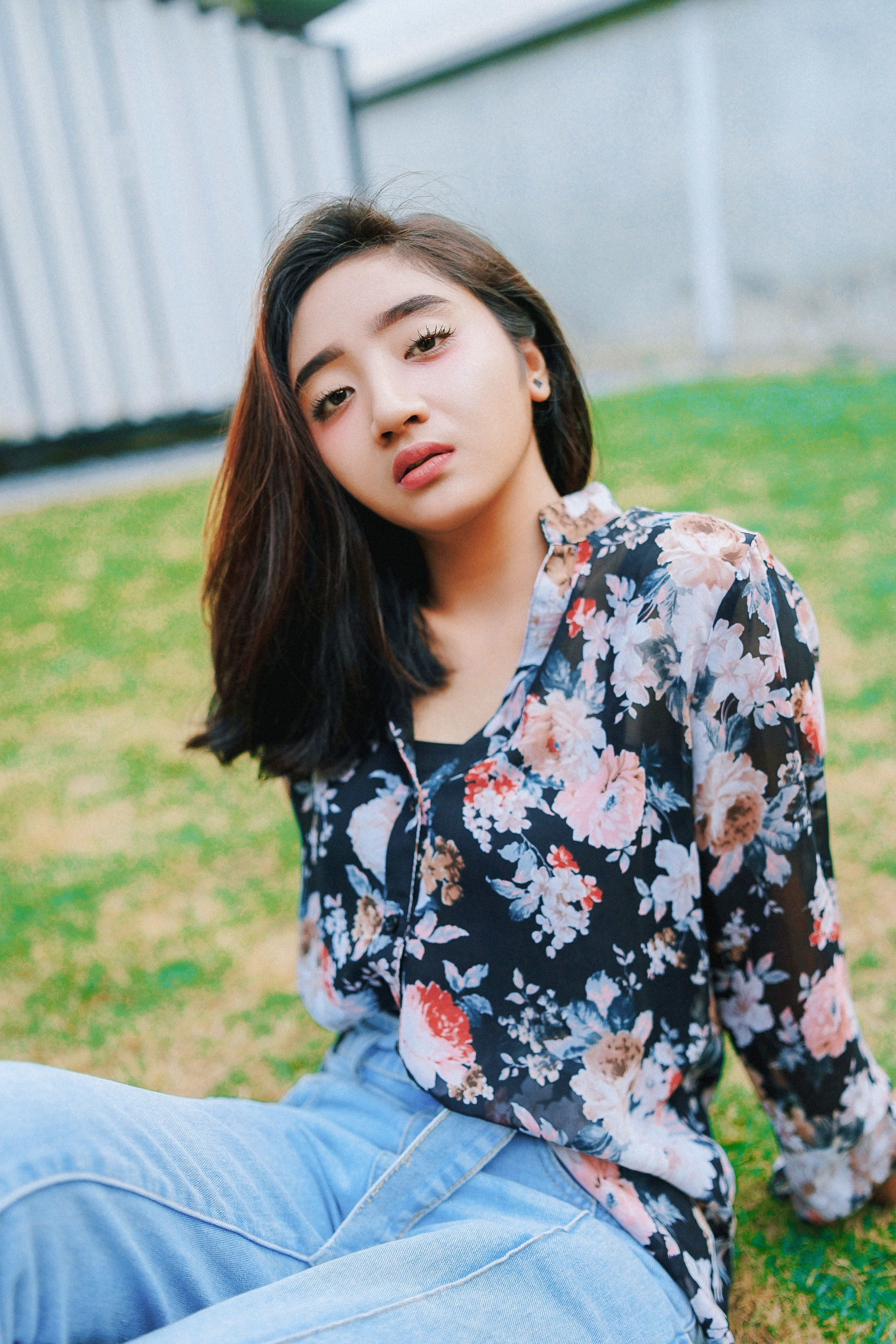一位年轻女子身着花卉衬衫和牛仔裤，坐在草地上