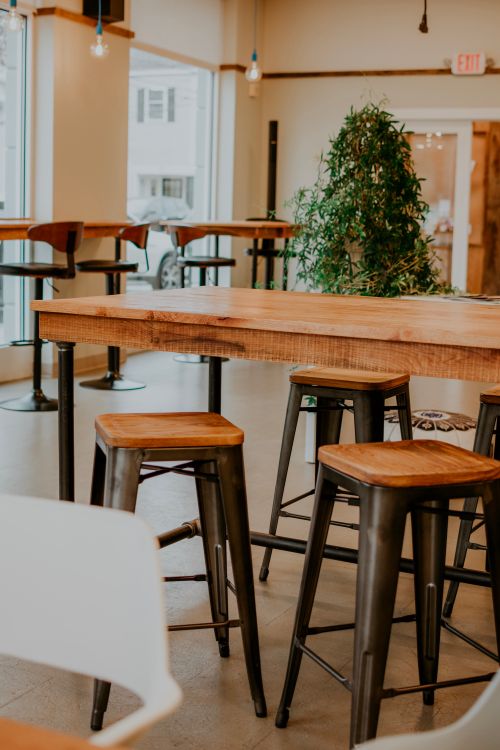 Free Contemporary restaurant interior featuring wooden tables and stools with natural light. Stock Photo