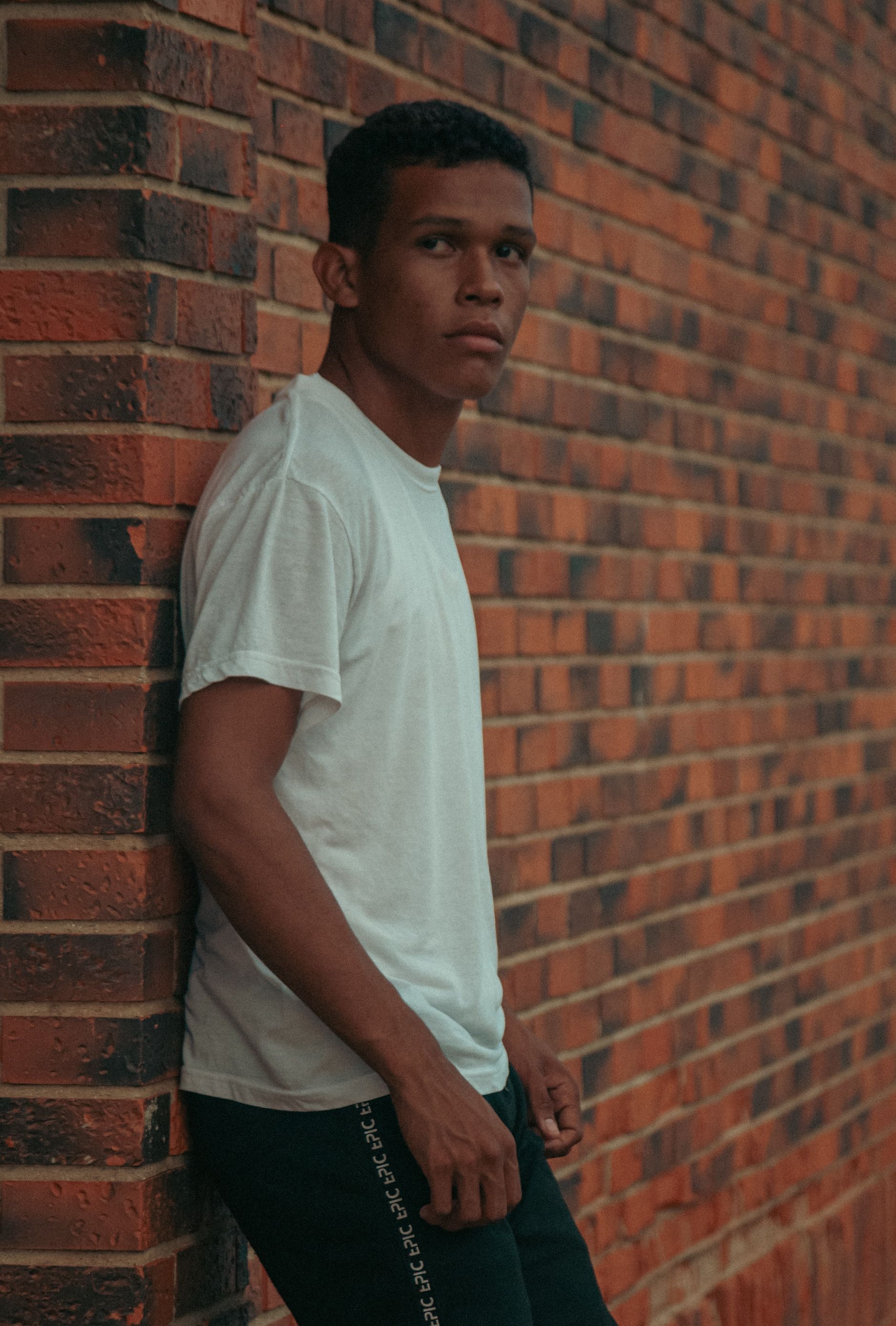 A young man leaning against a brick wall · Free Stock Photo