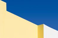 Abstract geometric yellow and white structures under a vibrant blue sky.