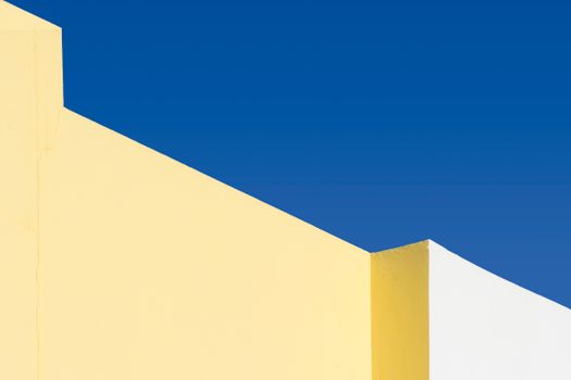 Abstract geometric yellow and white structures under a vibrant blue sky.