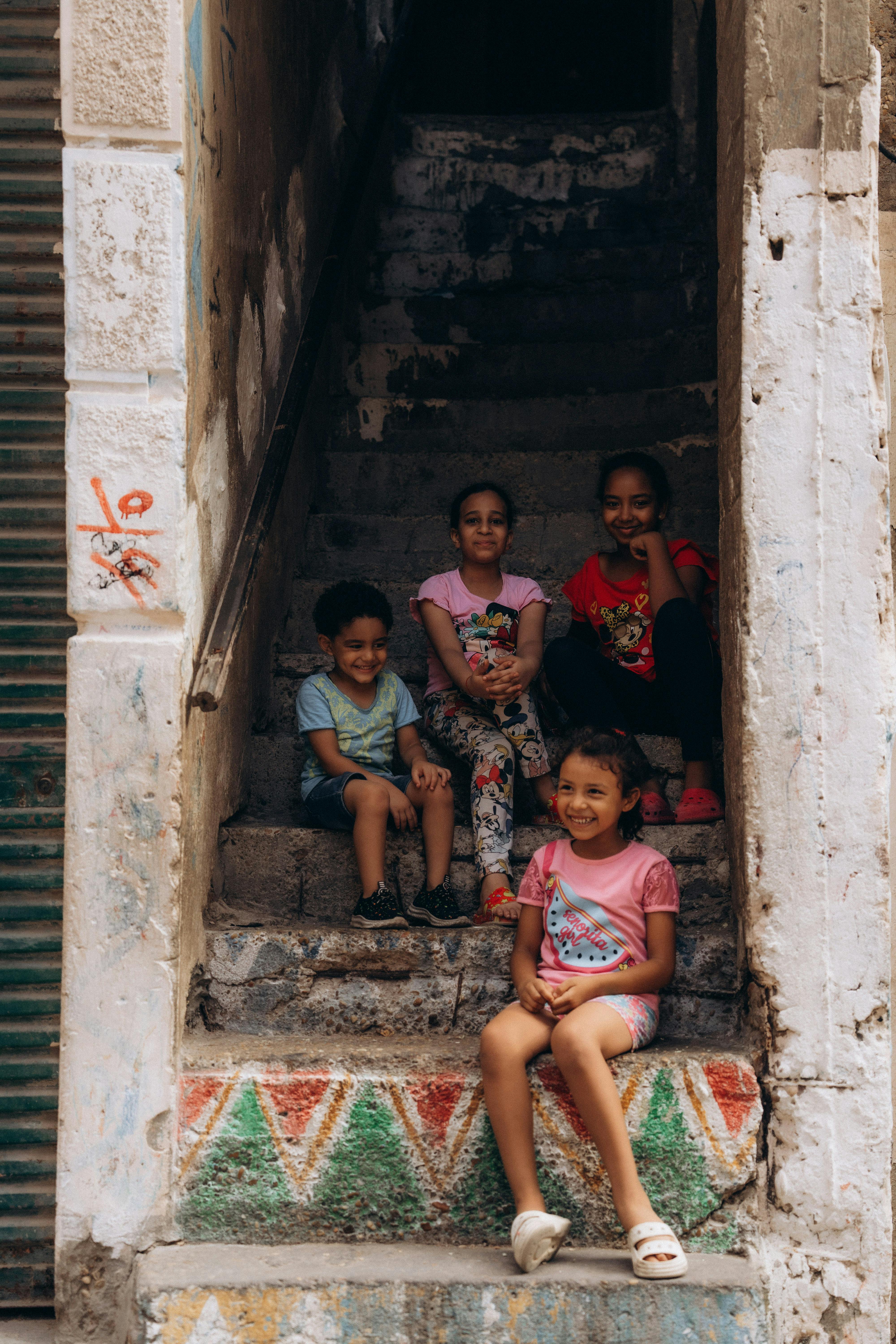 Four children sitting on decorated steps in Alexandria, Egypt, smiling at the camera.
