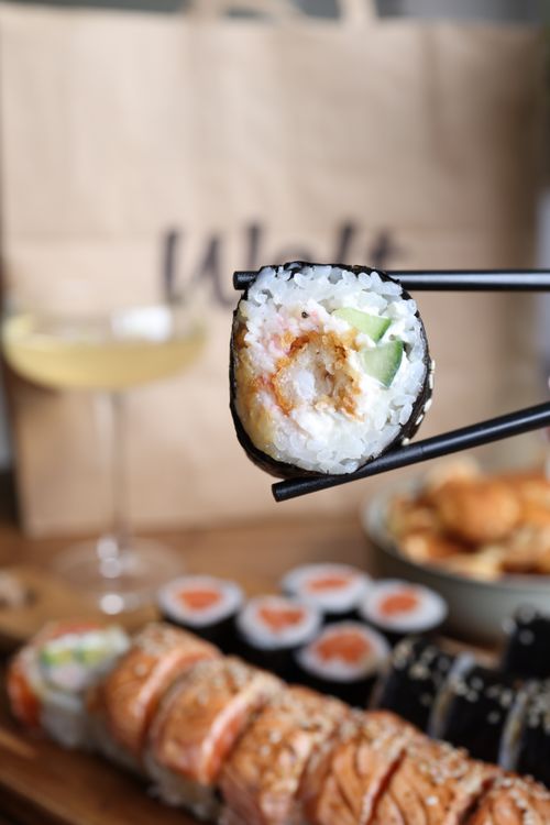 Free Detailed shot of sushi roll held by chopsticks with a table setting in the background. Stock Photo