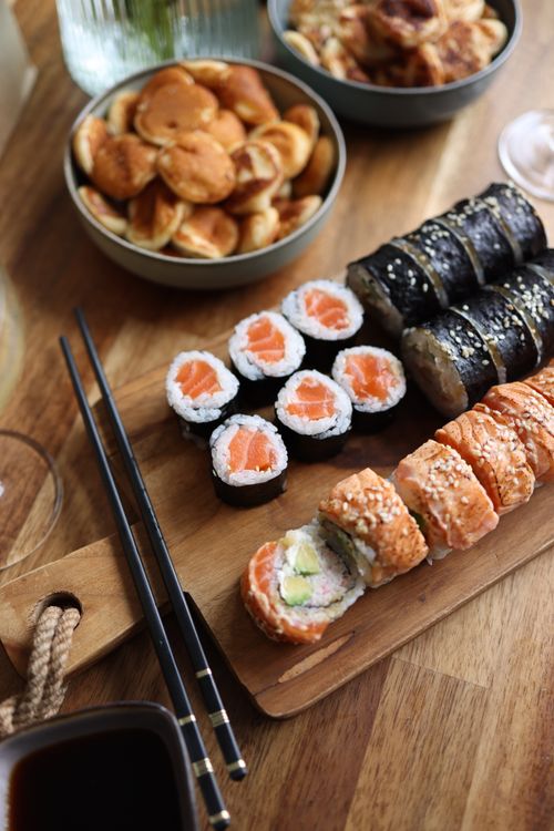 Free Assorted sushi rolls with salmon and avocado on a wooden platter, paired with snacks for an inviting meal. Stock Photo