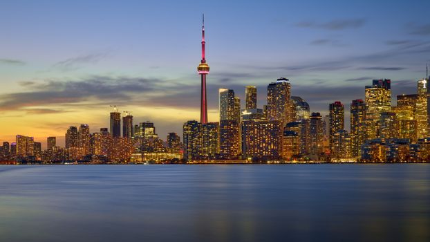 Vibrant Toronto skyline with CN Tower at dusk, reflecting over calm waters.
