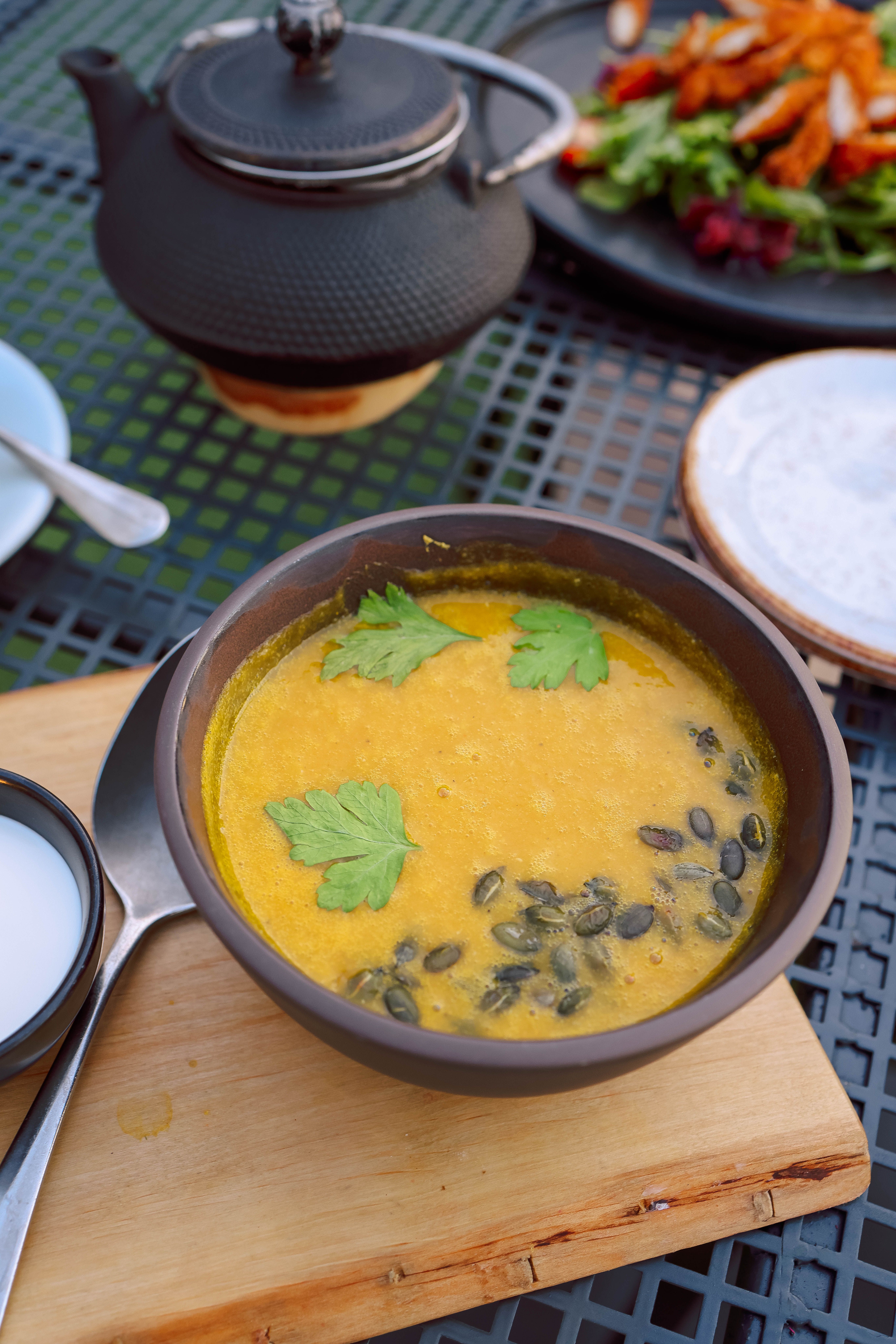 Delicious creamy pumpkin soup garnished with parsley and pepitas, served outdoors.