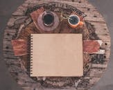 一张乡村桌子的顶视图，上面放着一本空白笔记本、咖啡和凉茶