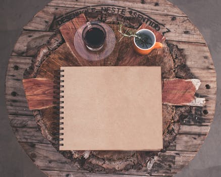 一张乡村桌子的顶视图，上面放着一本空白笔记本、咖啡和凉茶