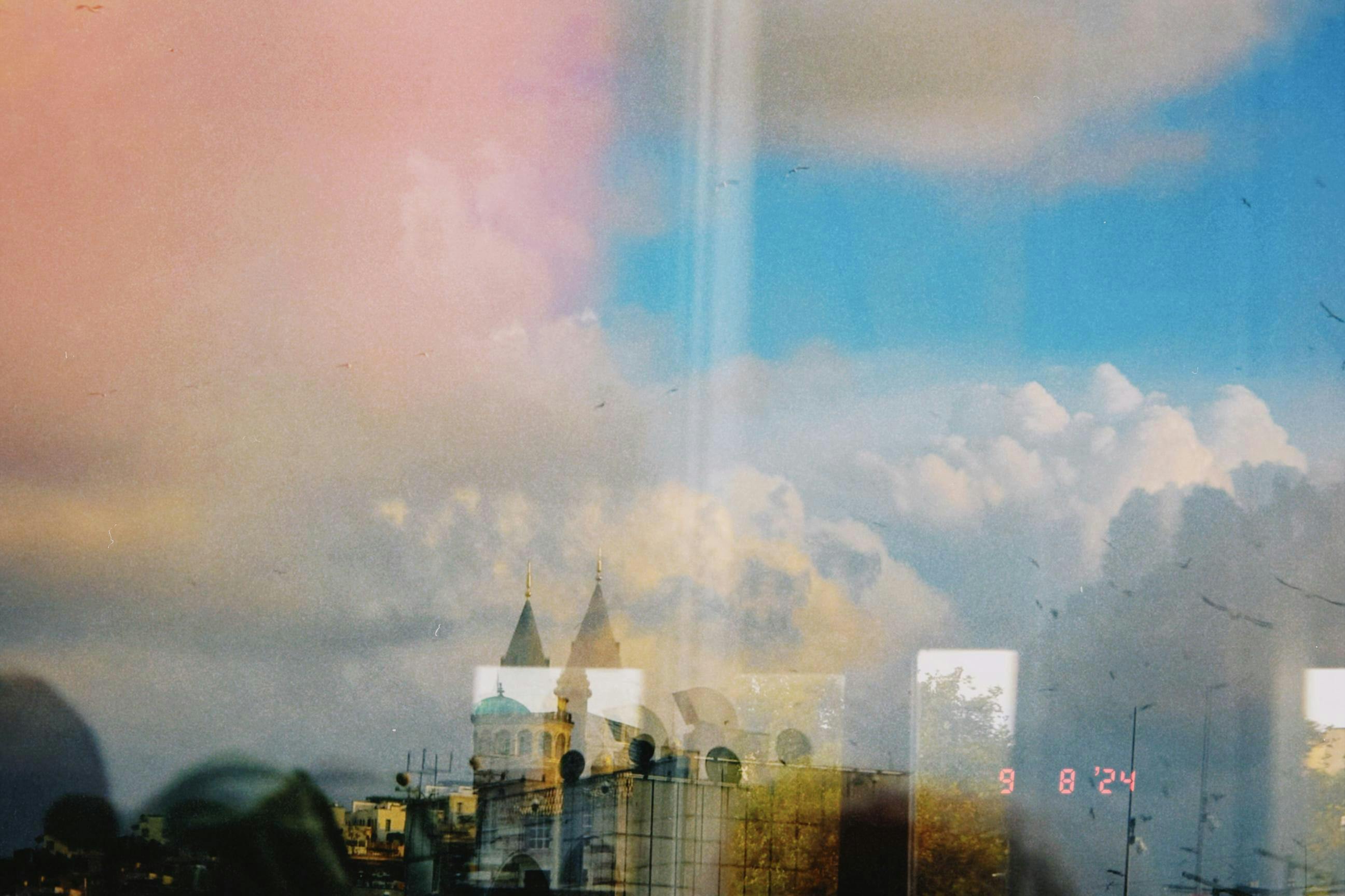 Double exposure of cityscape with towers against a pink and blue sky.