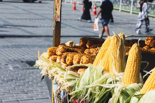 Fresh and grilled corn on display at an outdoor street market, attracting passersby.