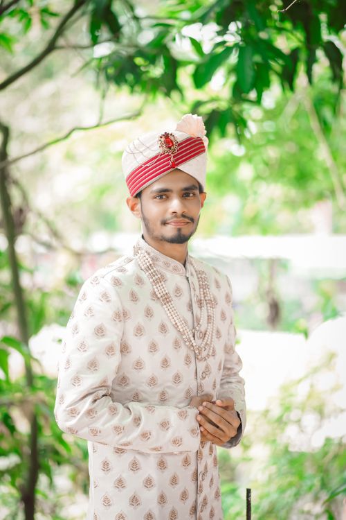 Free Young Bengali groom dressed in traditional attire posing outdoors with lush greenery. Stock Photo