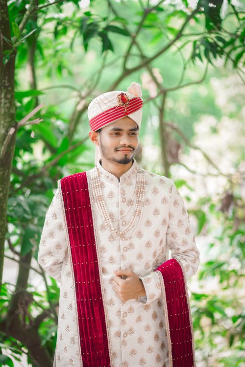 Free A smiling groom in classic Bengali wedding attire poses elegantly in a lush green park. Stock Photo