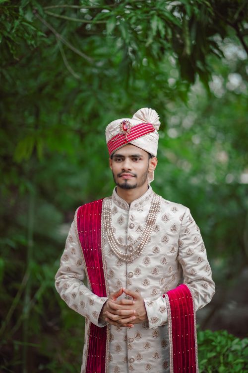 Free A Bengali groom in ornate traditional attire poses outdoors with lush greenery. Stock Photo