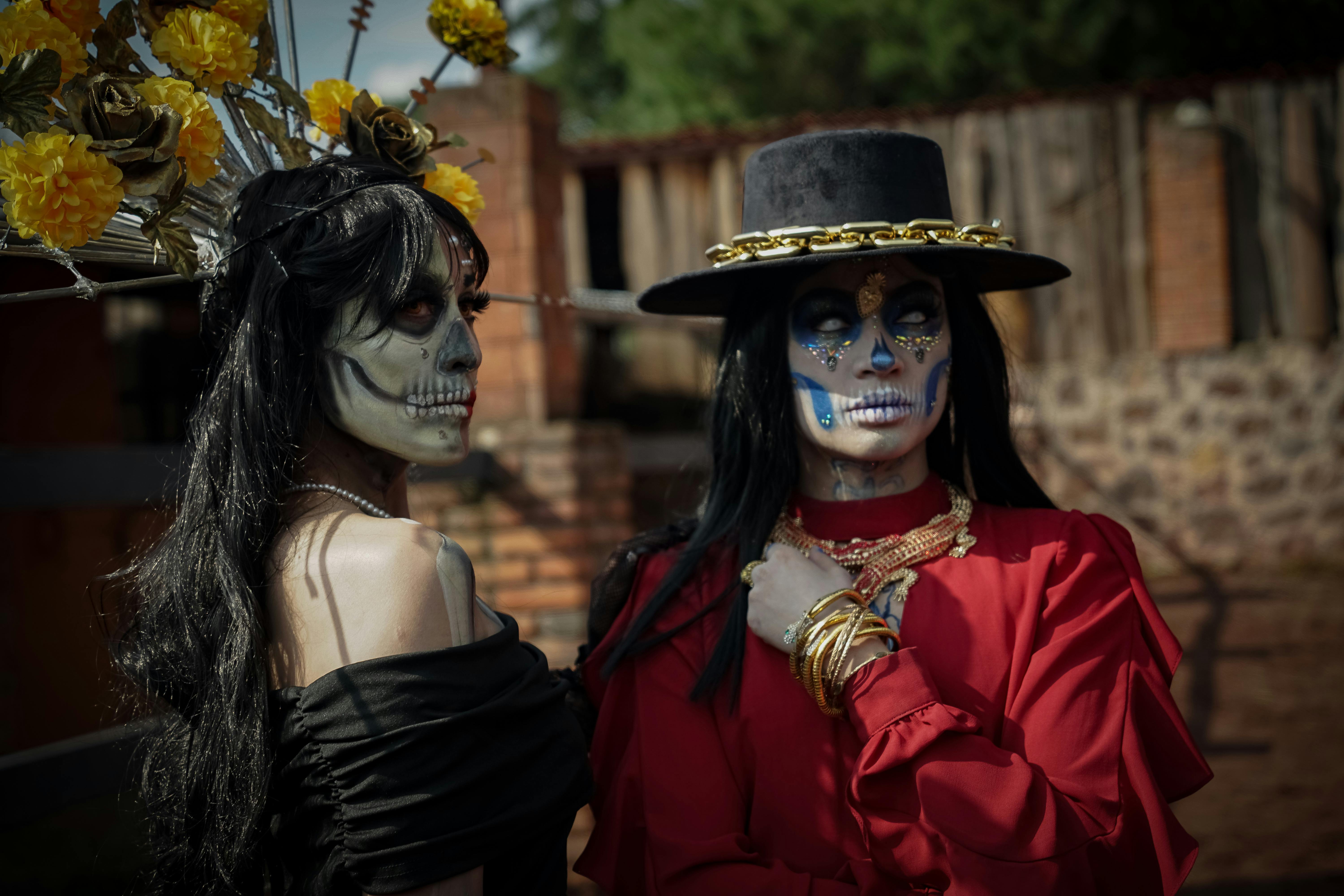 Two women in vibrant Day of the Dead costumes and makeup at an outdoor festival.