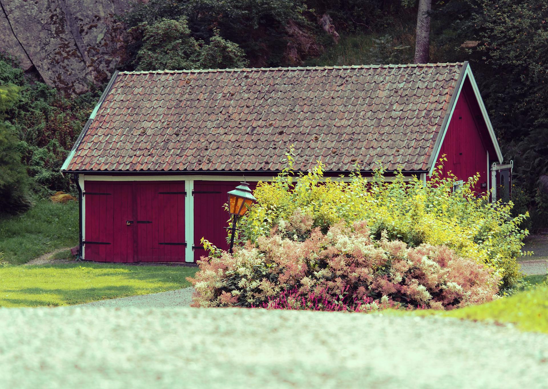 Charming red barn with a vintage roof surrounded by blooming garden in a lush countryside landscape.