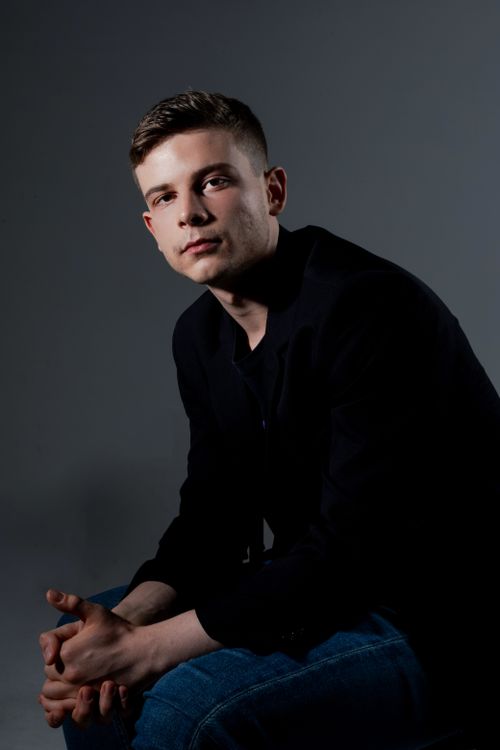 Free Captivating portrait of a young man seated in a studio with dramatic lighting, creating a pensive mood. Stock Photo