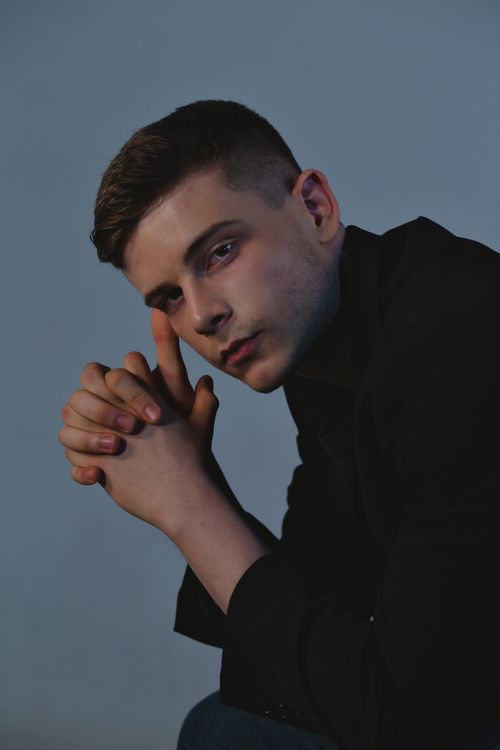 Free Contemplative young man with folded hands and serious expression in dimly lit studio setting. Stock Photo