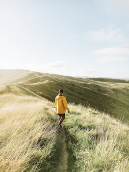 一个穿着黄色夹克的男人，在阳光明媚的日子里沿着草山徒步，捕捉着冒险与自然的瞬间