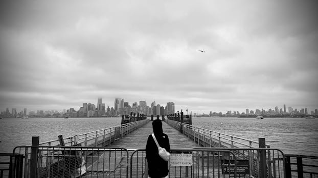 A black and white view of New York City skyline from a foggy pier, capturing a moody atmosphere.