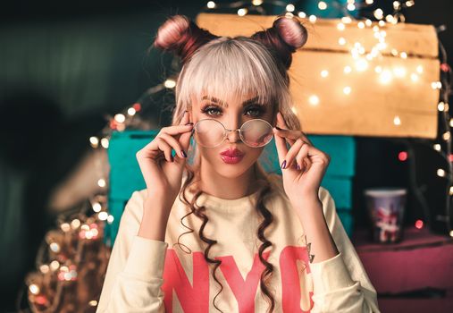 Trendy woman with bangs posing indoors with eyeglasses and playful hairstyle.