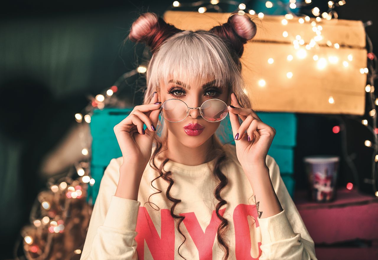 trendy woman with bangs posing indoors with eyeglasses and playful hai