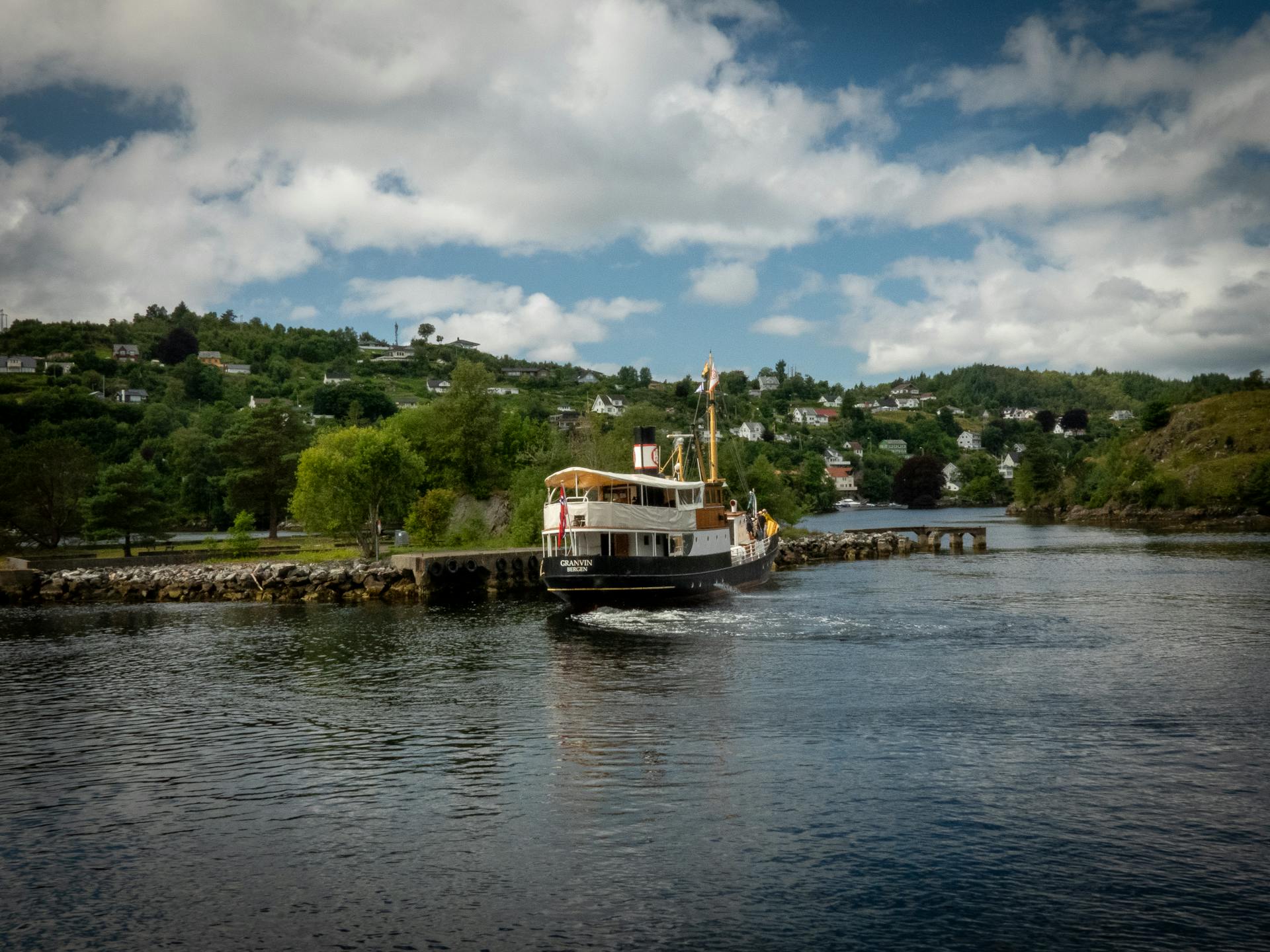 A serene boat cruising through picturesque Norwegian fjords under a bright blue sky.