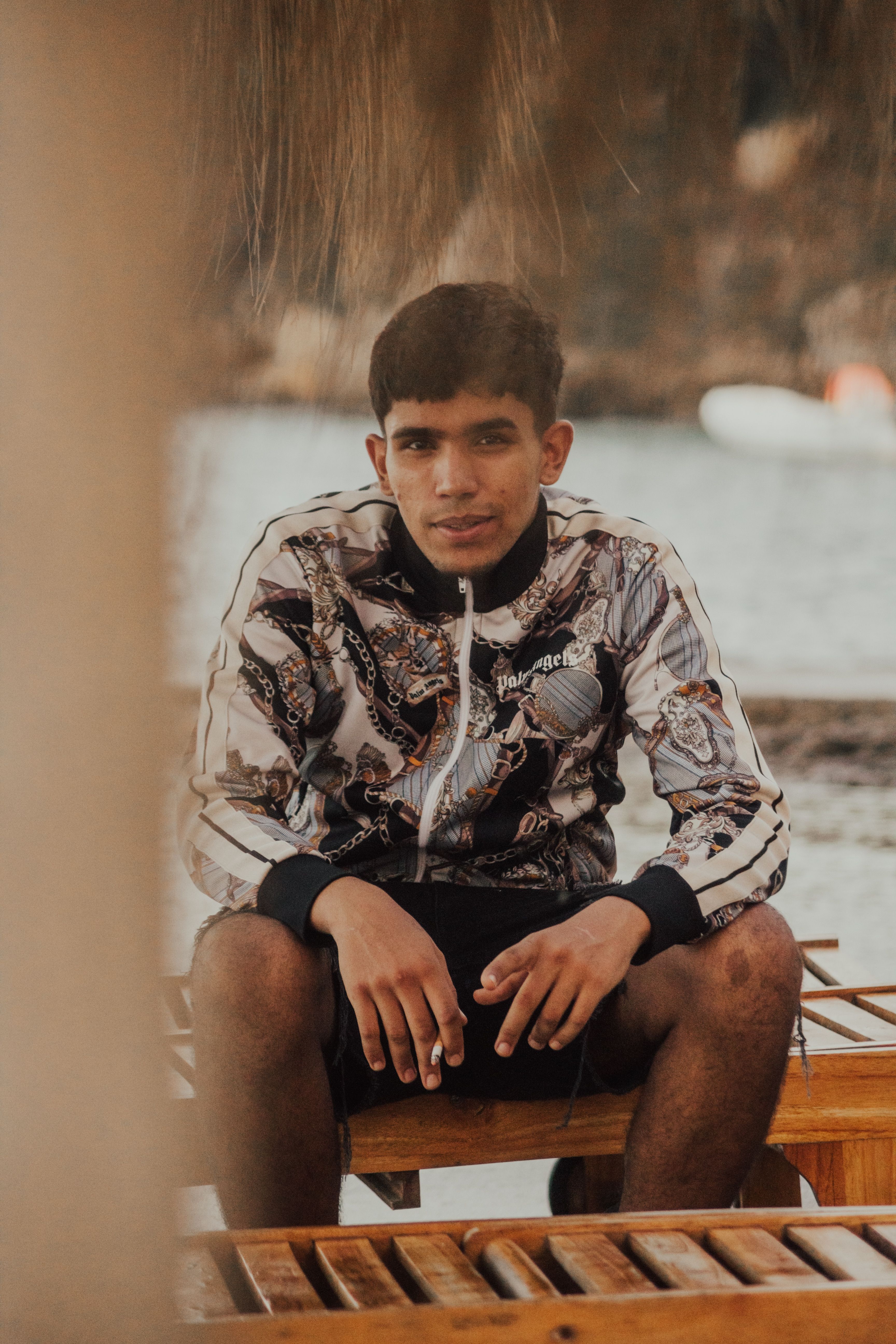 A young man in a stylish jacket sits on an outdoor bench, exuding a cool vibe.