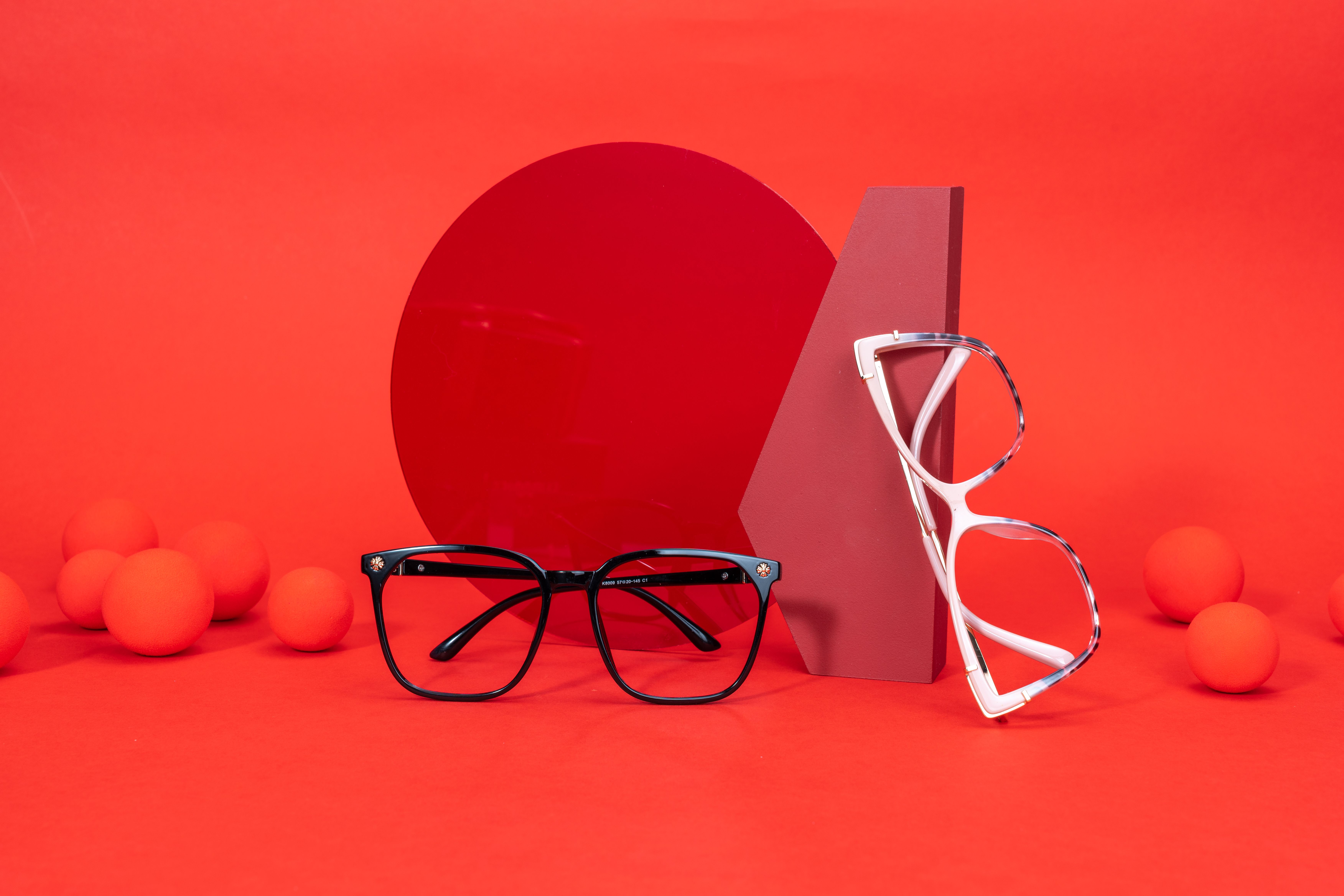 Óculos modernos com uma configuração artística única sobre um fundo vermelho vibrante.