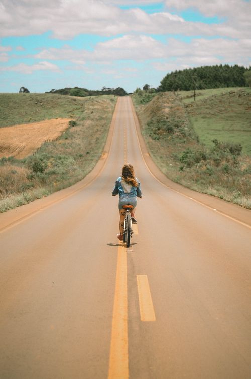 Free A blonde girl rides a bicycle down a long scenic highway surrounded by countryside fields. Stock Photo