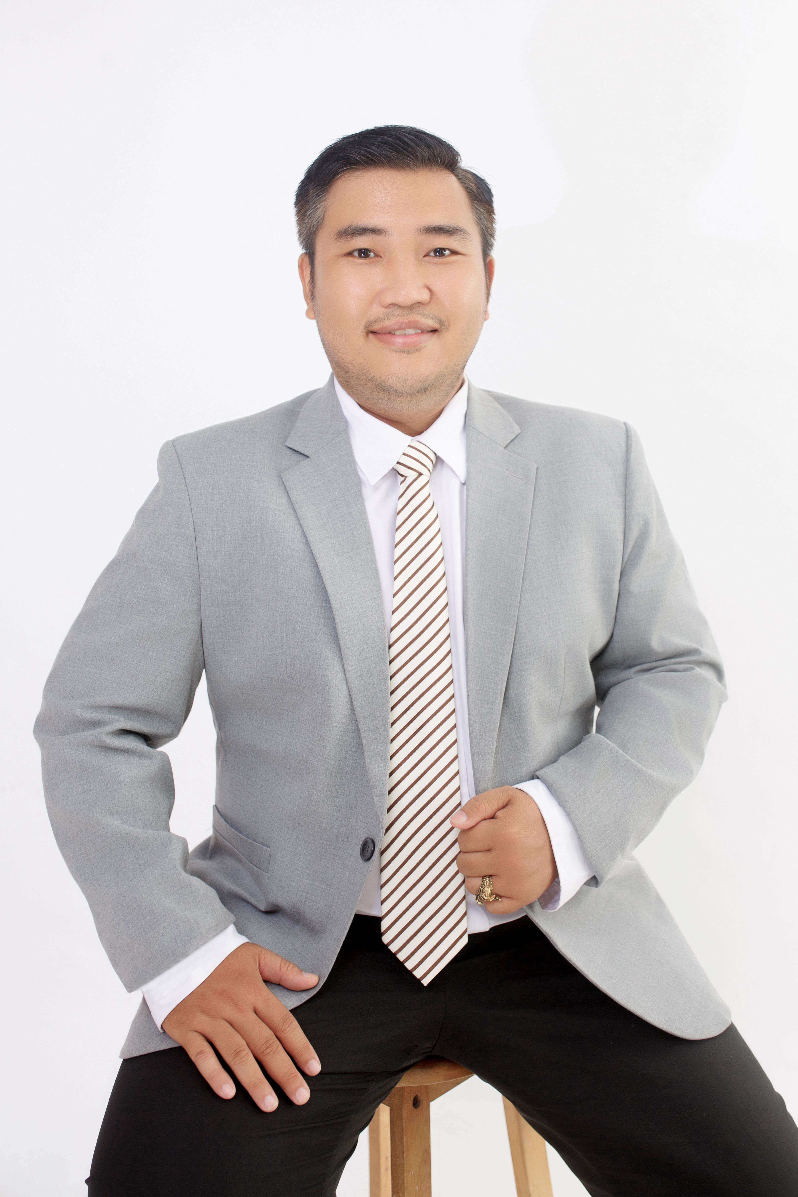 Portrait of a confident businessman in a grey suit with a striped tie, seated on a stool.