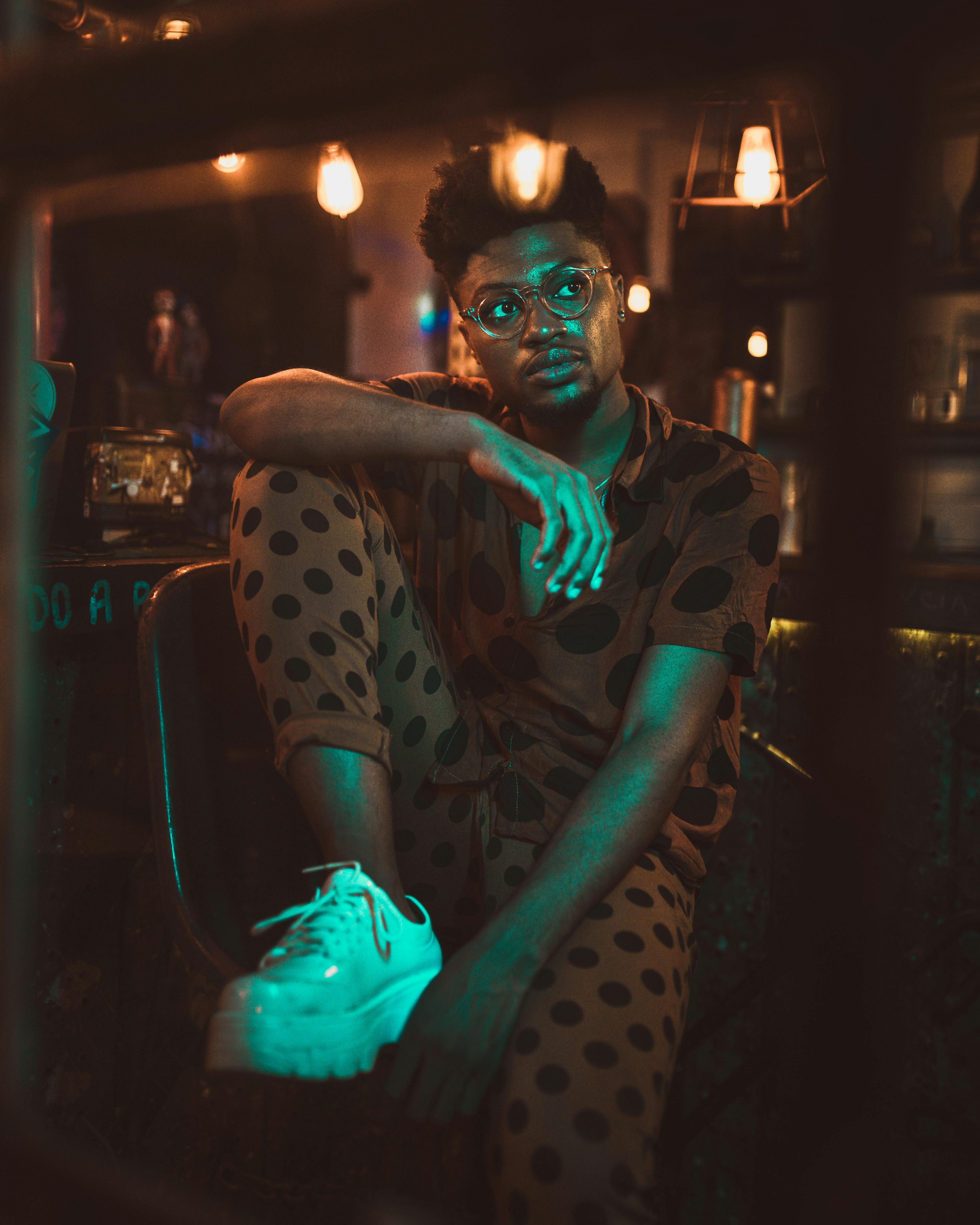 一位衣着时尚、戴着眼镜的男士坐在室内，被温暖的光线笼罩