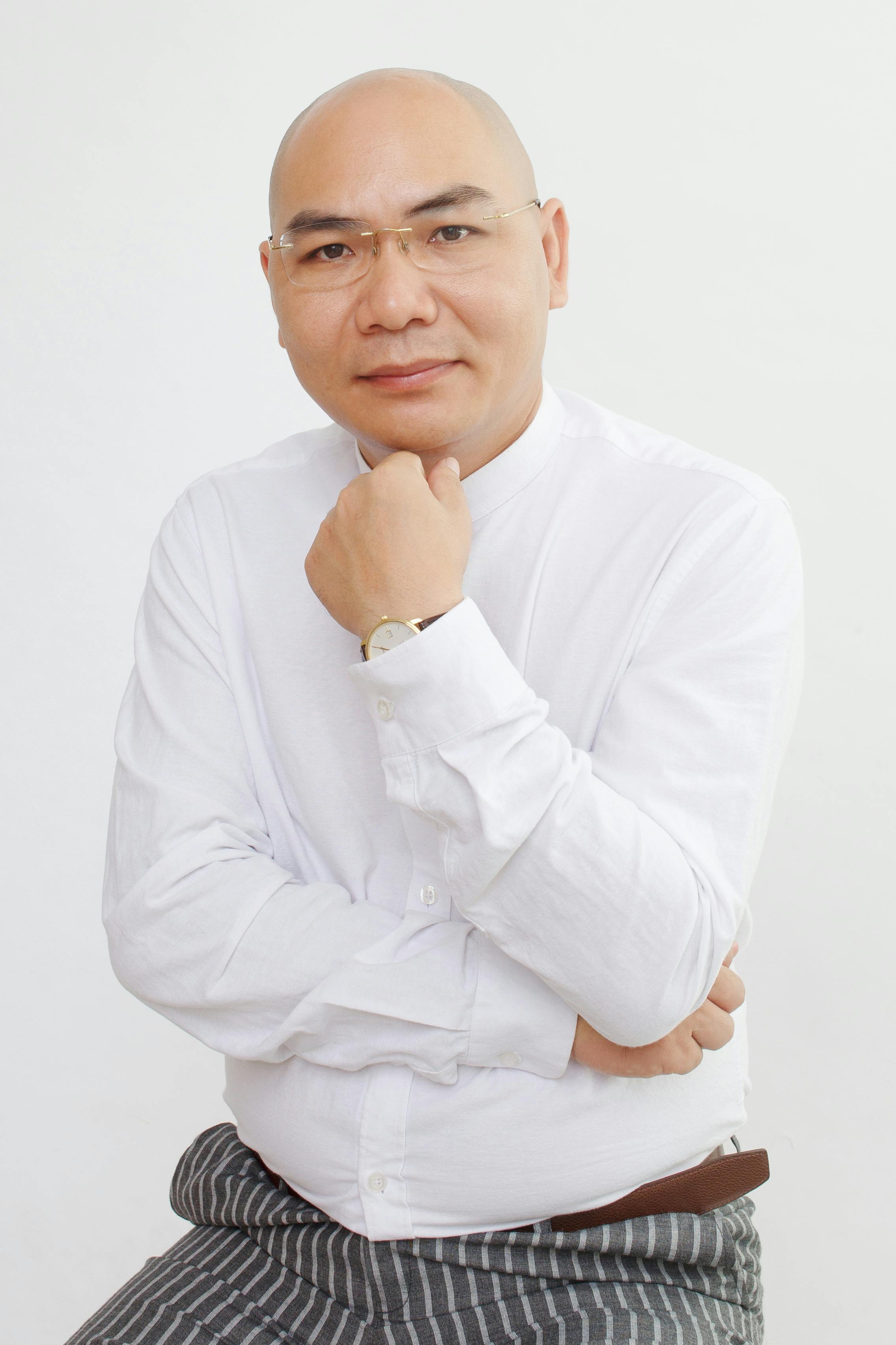 Portrait of a bald Asian man in a white shirt, exuding confidence and intelligence.