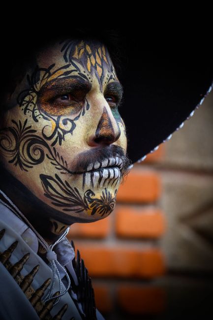 Close-up portrait of a man in traditional Día de Muertos face paint and sombrero.